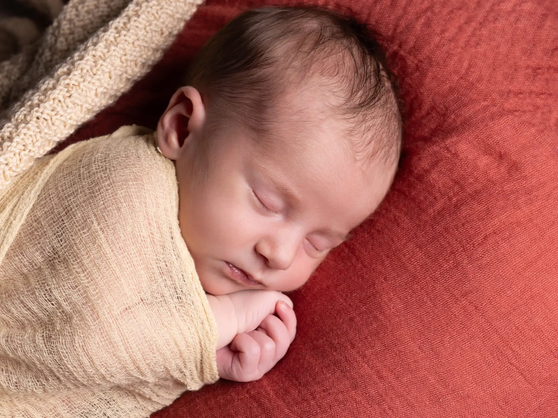 Bébé endormi enveloppé dans des langes beige, posé sur un tissu doux, douceur et chaleur naturelle.