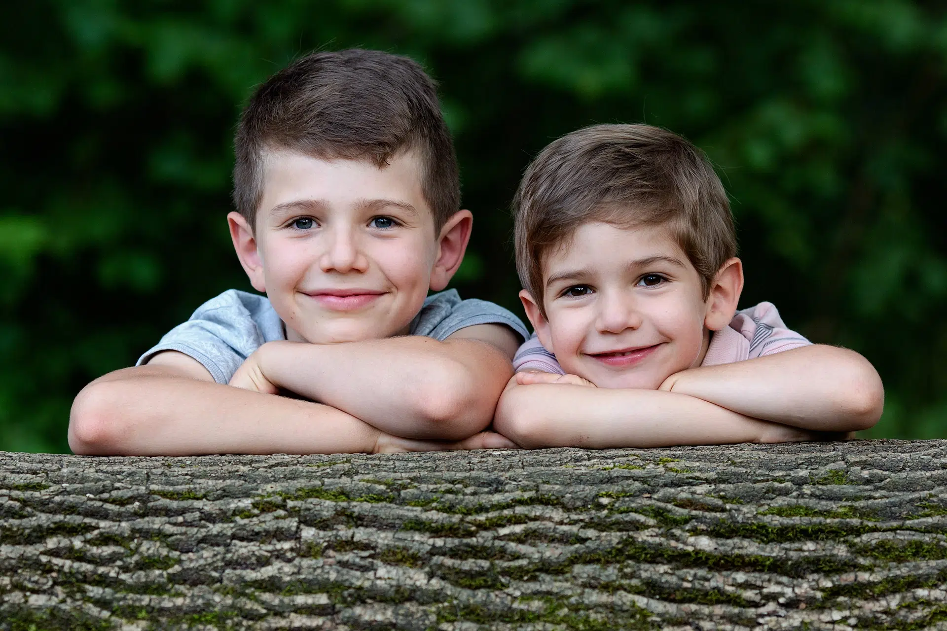 Deux jeunes garçons souriants appuyés sur une gouttière en bois en extérieur, ambiance naturelle et lumineuse.