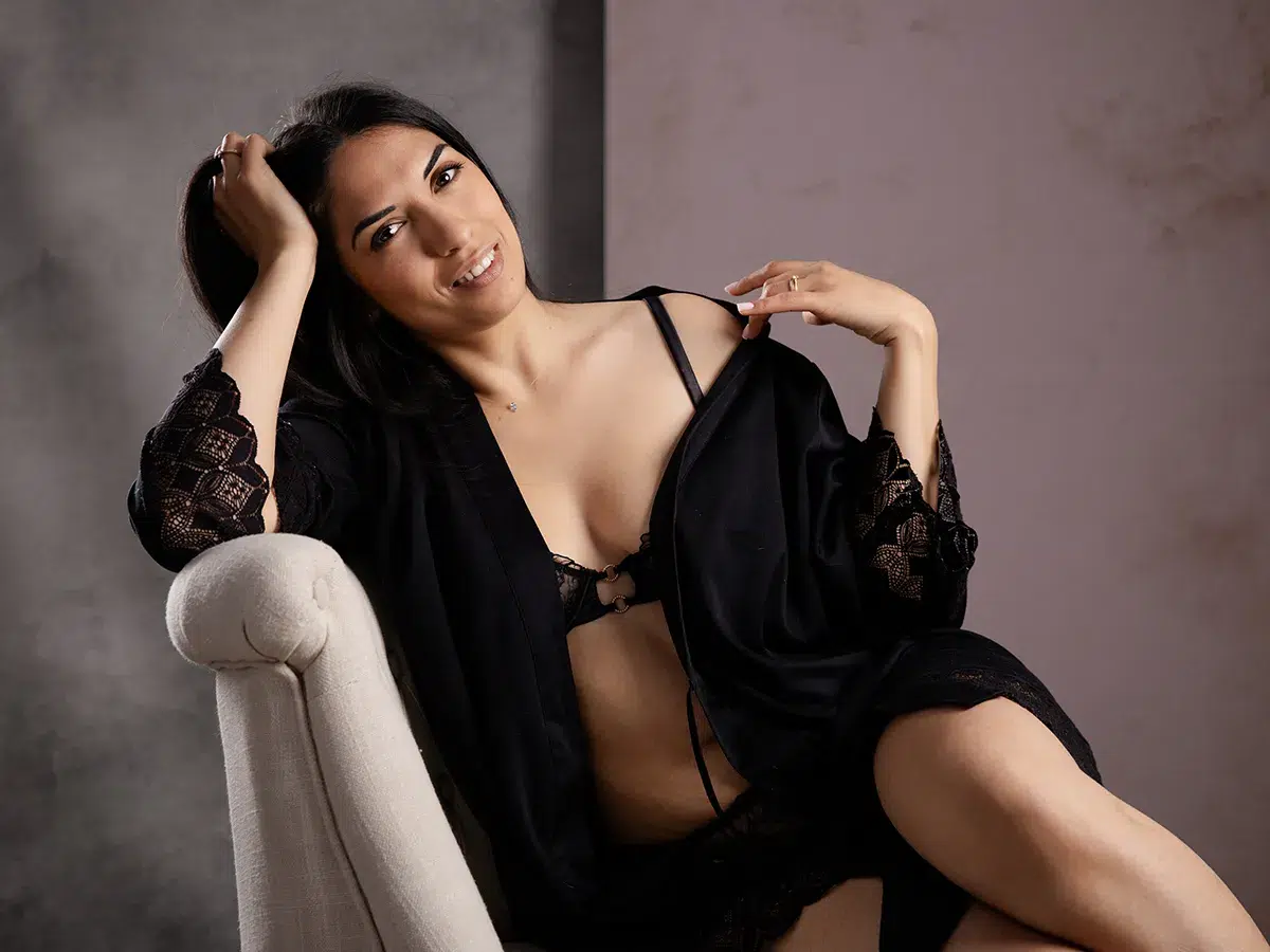 Jeune femme en déshabillé noir sur un fauteuil beige