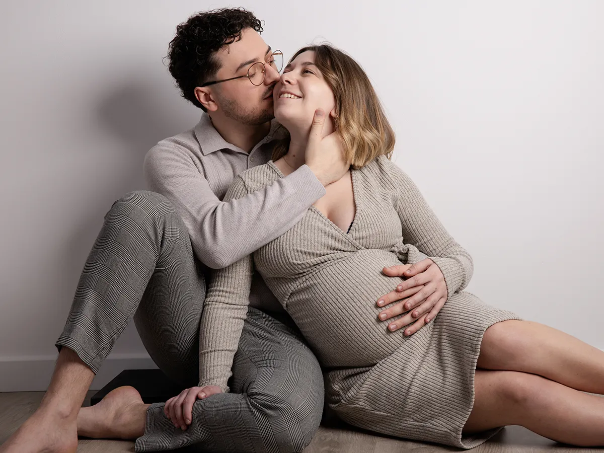 Couple lors d'une séance grossesse, assis au sol. ils s'embrassent.