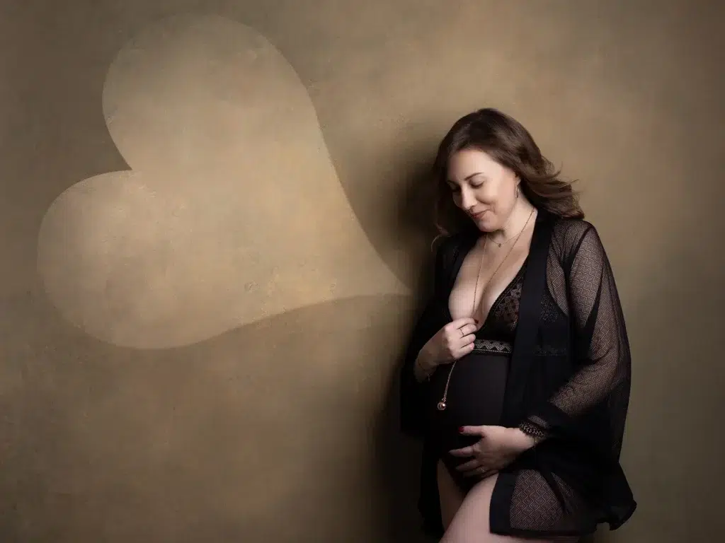 Femme enceinte en robe légère, se tenant le ventre dans une atmosphère douce, avec un cœur flou en arrière-plan. baby shower idée intégrée naturellement.