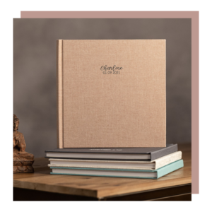 Album ou livre photo en carton beige posé sur des livres, avec le nom "Charline" et la date imprimés dessus.