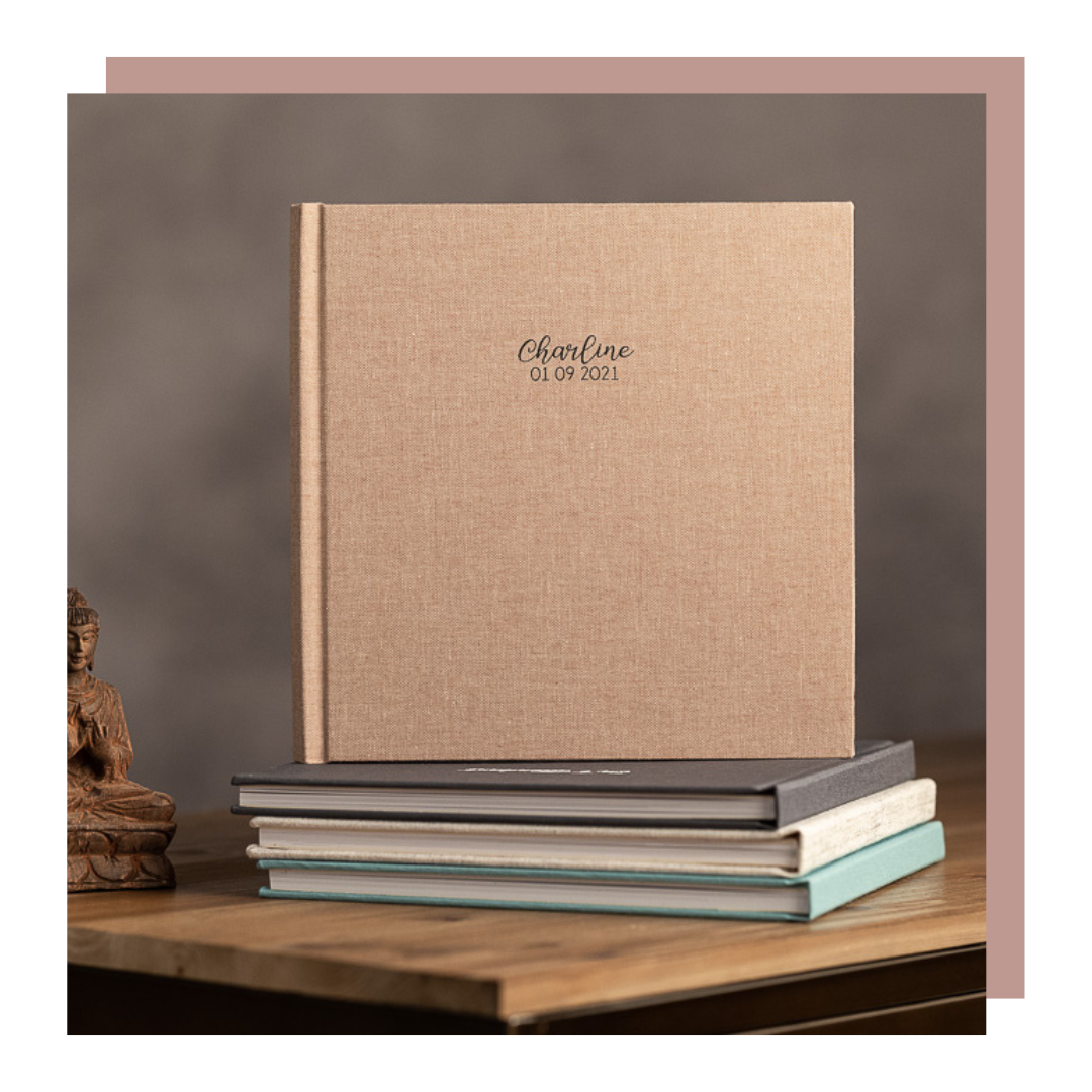 Album ou livre photo en carton beige posé sur des livres, avec le nom "Charline" et la date imprimés dessus.